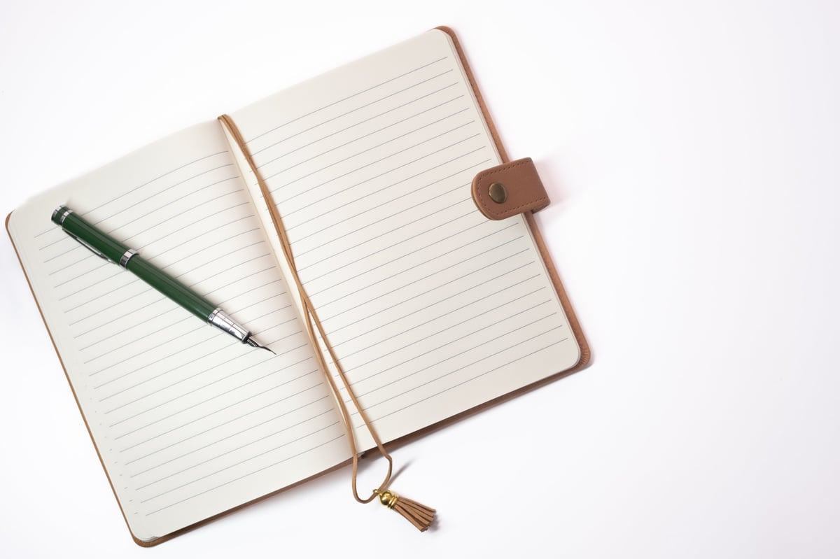 An open notebook with a pen on a wooden desk